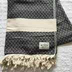 These Turkish throws have a stylish complex weave and are suited to use indoors and outdoors The incredibly soft hand-feel of these throws is truly luxurious! They are woven in a reversible black pattern and have a creme border complementing creme, and hand-spun tassels on the top and bottom edges. Large Throw: 55 inches X 78 inches 100% Turkish cotton