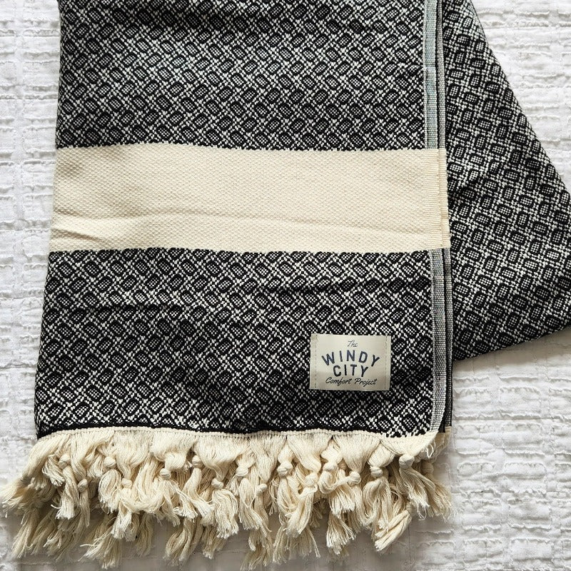 These Turkish throws have a stylish complex weave and are suited to use indoors and outdoors The incredibly soft hand-feel of these throws is truly luxurious! They are woven in a reversible black pattern and have a creme border complementing creme, and hand-spun tassels on the top and bottom edges. Large Throw: 55 inches X 78 inches 100% Turkish cotton