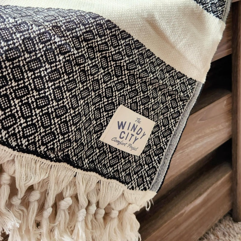 These Turkish throws have a stylish complex weave and are suited to use indoors and outdoors The incredibly soft hand-feel of these throws is truly luxurious! They are woven in a reversible black pattern and have a creme border complementing creme, and hand-spun tassels on the top and bottom edges. Large Throw: 55 inches X 78 inches 100% Turkish cotton